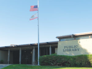 Willows civic building with United States and California flags on flagpole with Public Library sign to the right