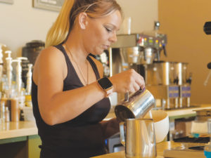 A woman preparing an espresso drink with cafe equipment in the background